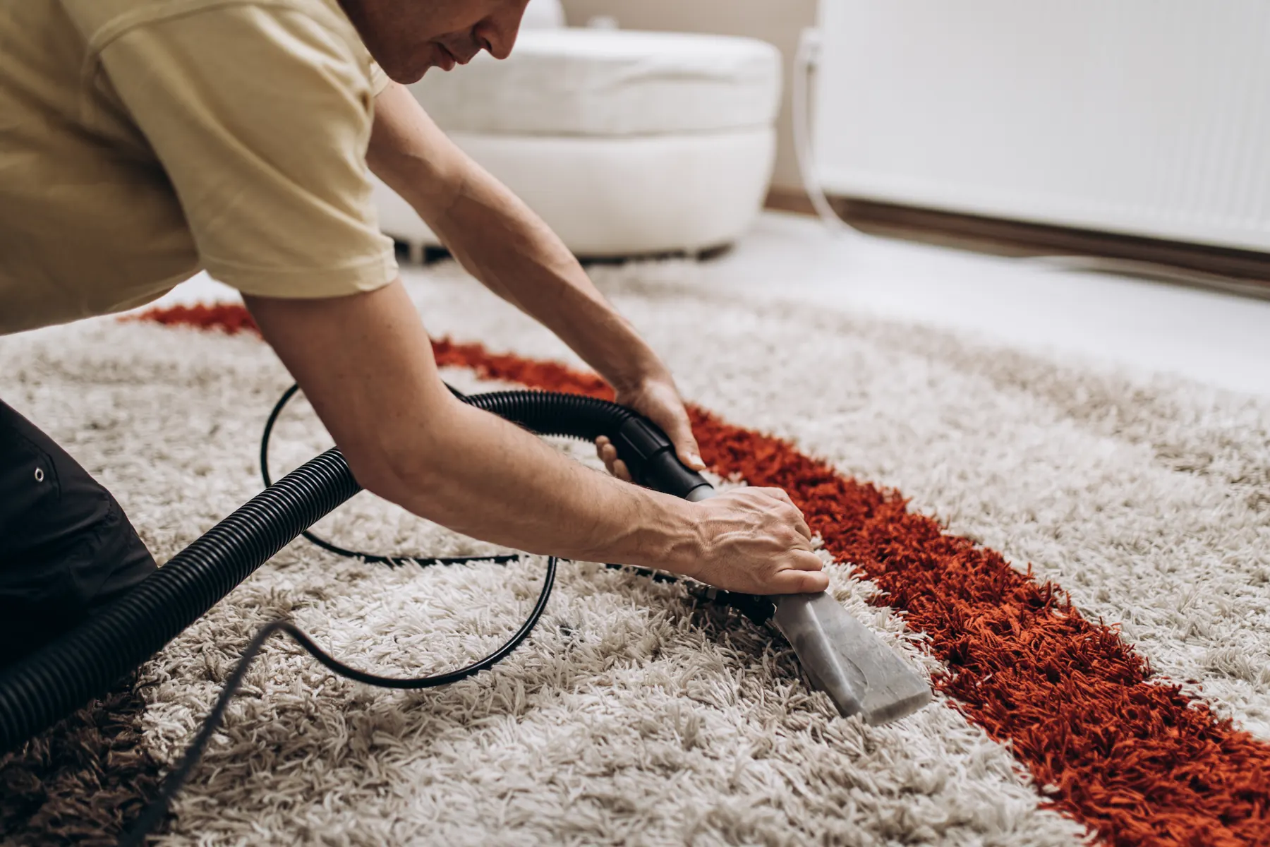 A man kneeling to run a hand held extraction tool across a cream shag rug