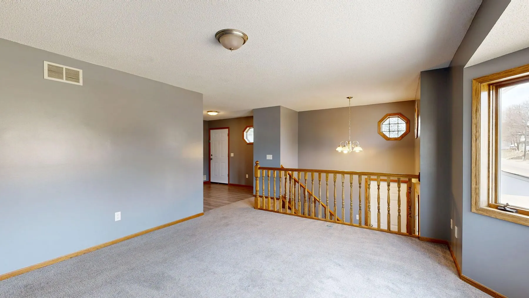 An empty upstairs landing with grey broadloom, a wooden stair railing and the front door below