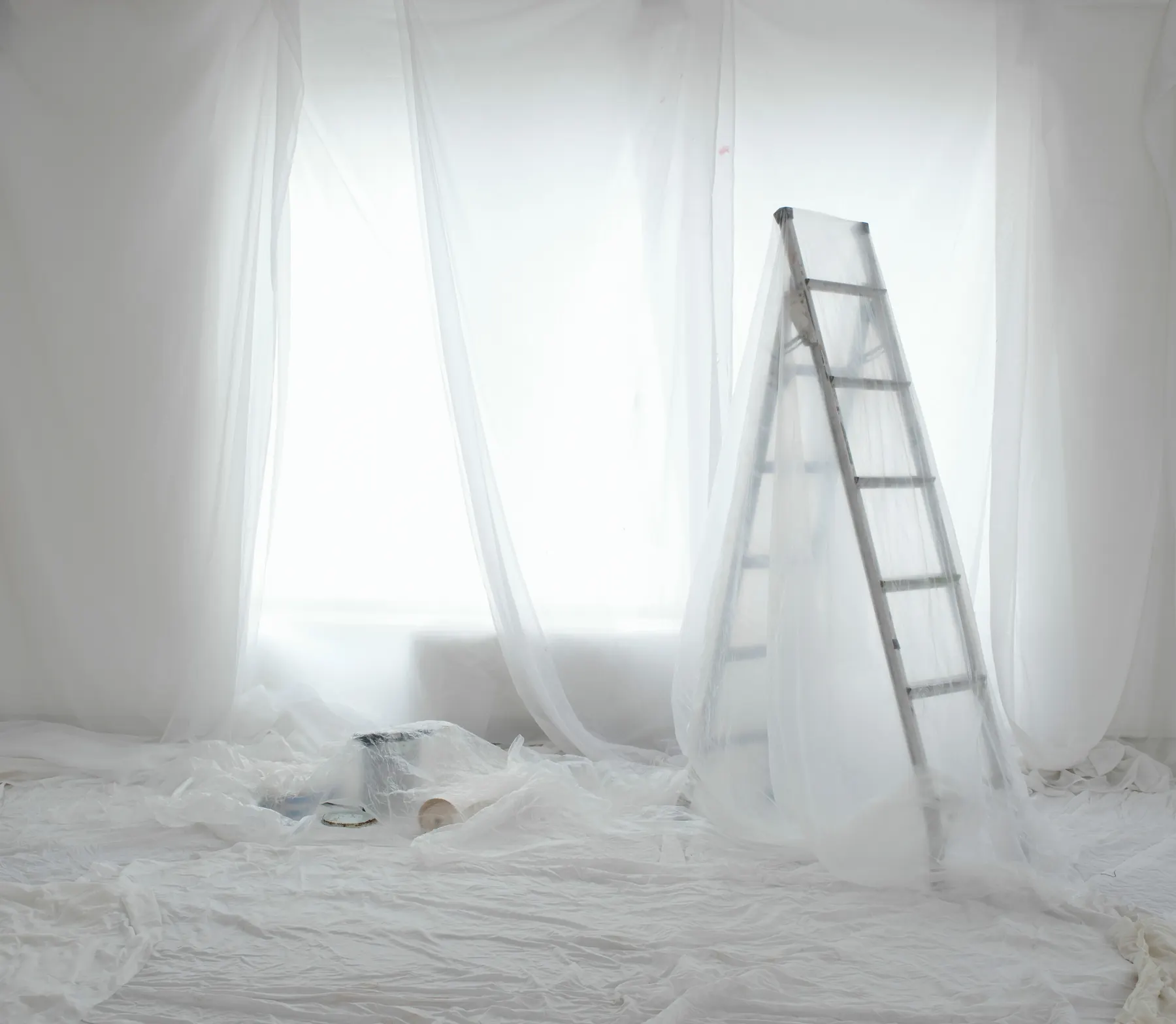 Polythene sheeting draped over a window and taped across the floor of a stripped room