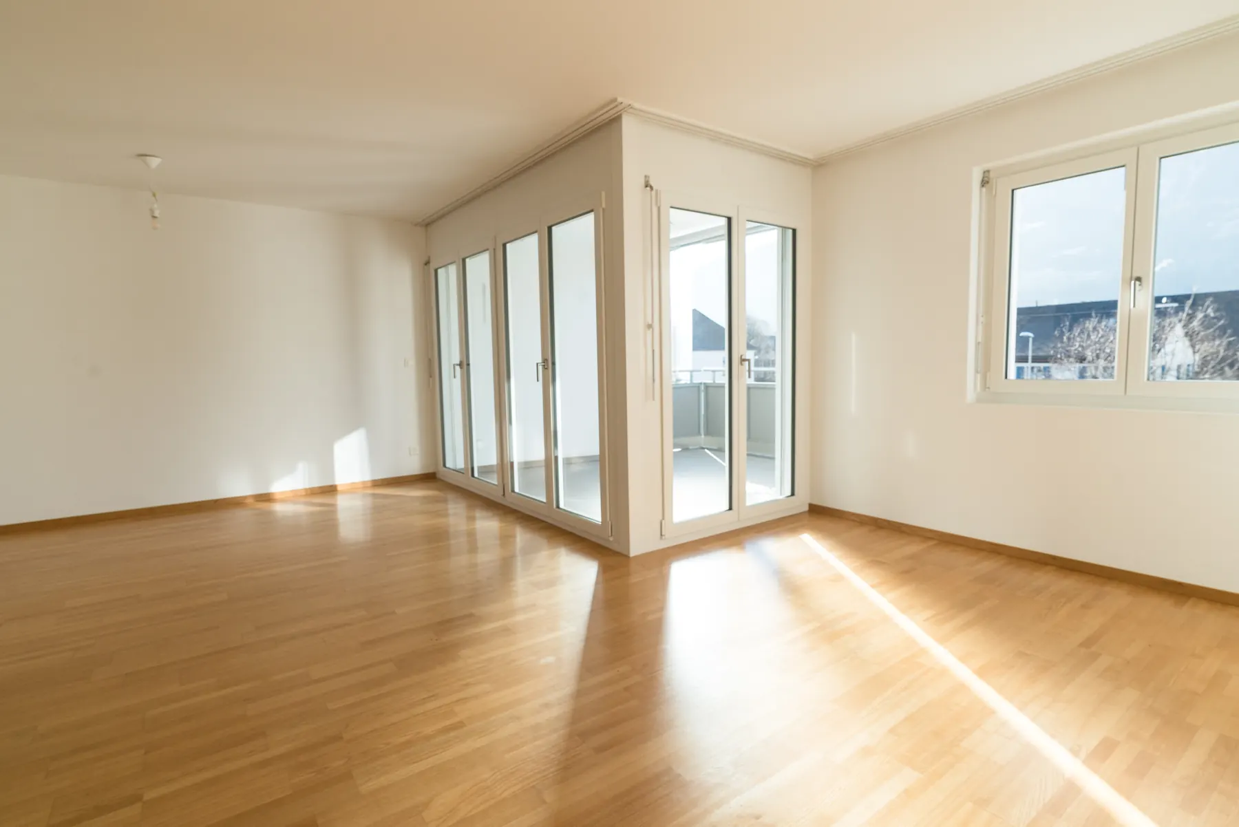 Empty room with pale strip wood flooring, white walls and full height glazed doors onto a balcony