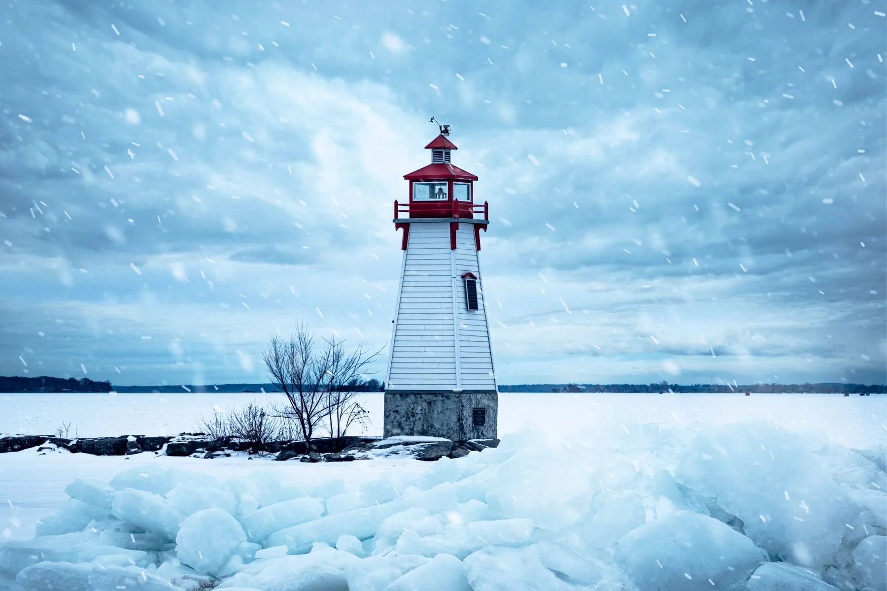 A white lighthouse with a red lantern on the frozen shore of Lake Simcoe in a snowstorm