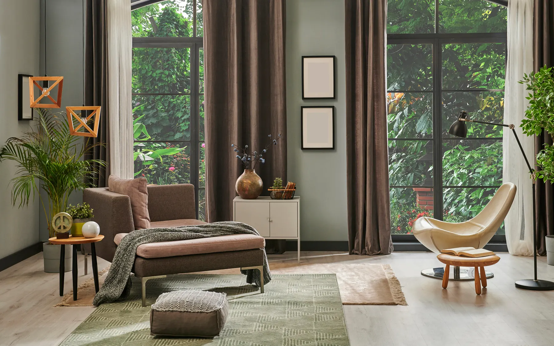 A furnished lounge with sage green walls, a brown velvet chaise, a green flat weave rug and a jute rug over pale wood-look flooring