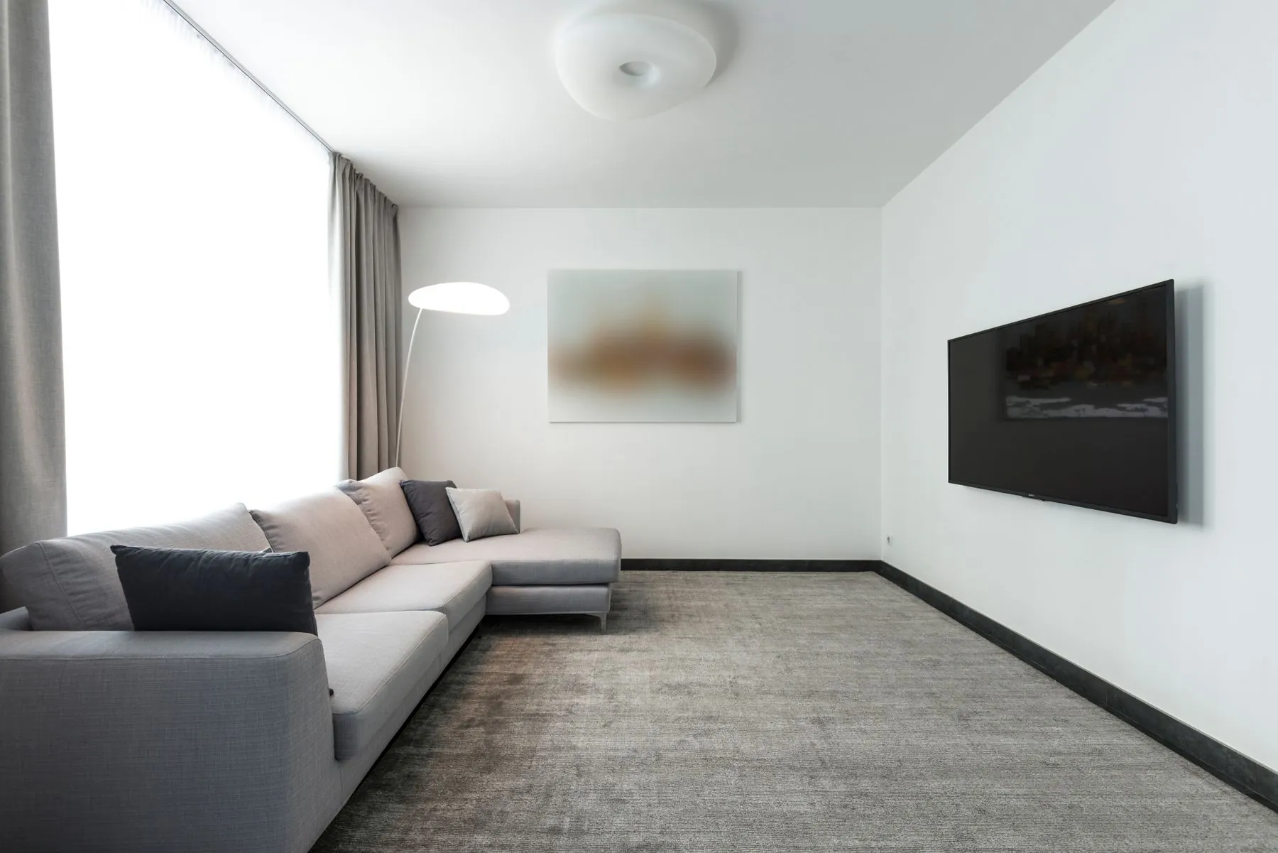A bright living room with a pale grey sectional sofa and a large grey patterned rug