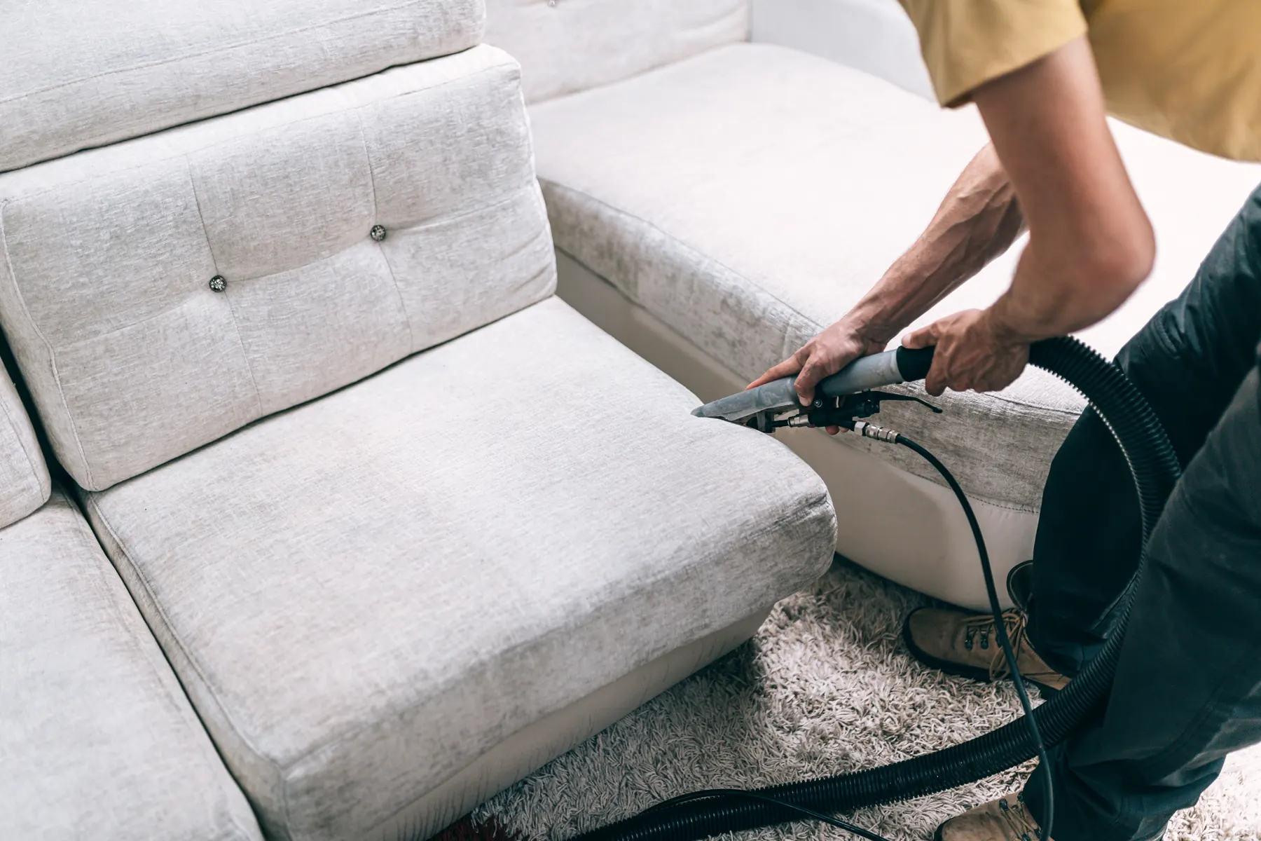 A gloved hand drawing an upholstery extraction tool across a grey fabric sofa cushion